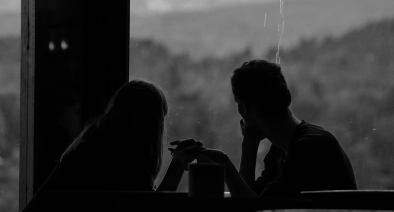 grayscale photography of couple sits by the window